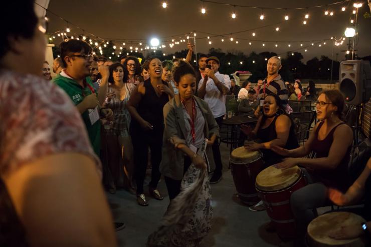 A woman dances in a circle of people as other women play drums