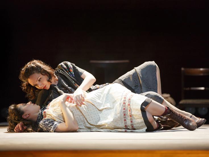 Two female actors lie together on stage