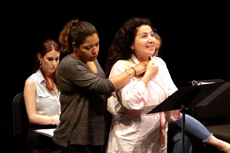 Two women embrace on stage in front of a music stand.