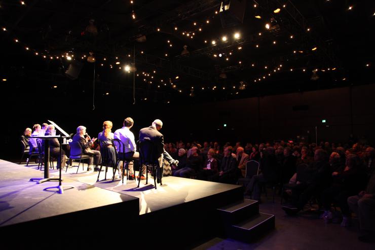 a line of people sit onstage facing an audience