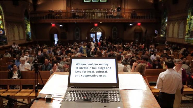 picture of a laptop screen with an audience in the back