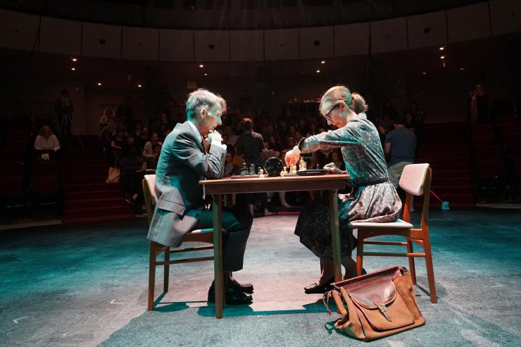 A man and a woman play chess on stage
