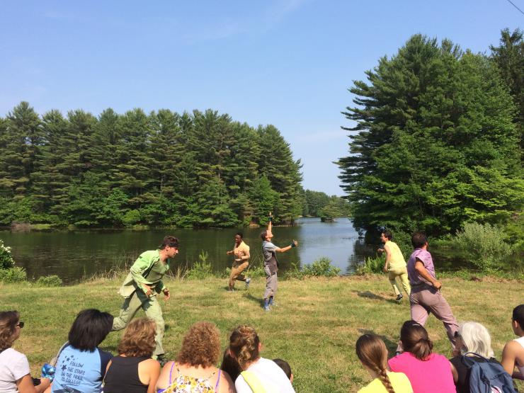 Five people performing in front of a lake