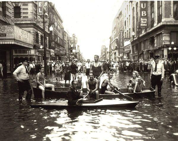 some people in boats, some people stand in a flooded street