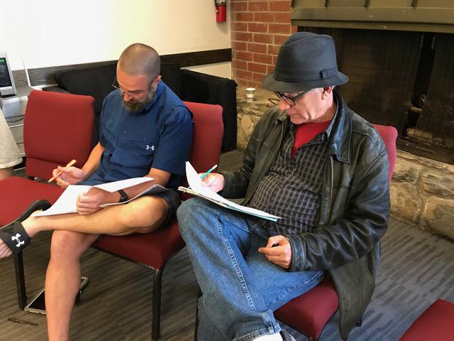 Two men sit and look at scripts