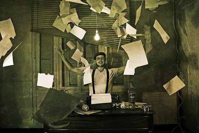 A man seated at a table tossing pages into the air.