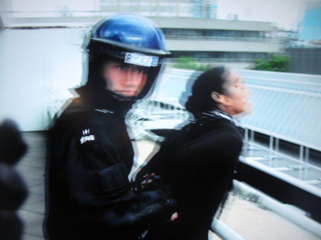 A cop in riot gear handcuffing a woman