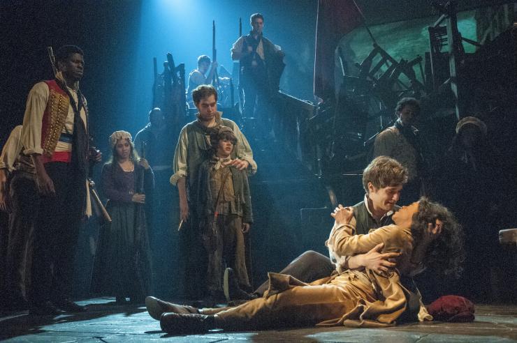 The cast of Les Mis on stage behind one actor sitting and cradling another in their lap.