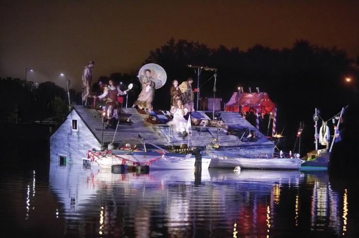 A house submerged in water with several actors standing on top of it.