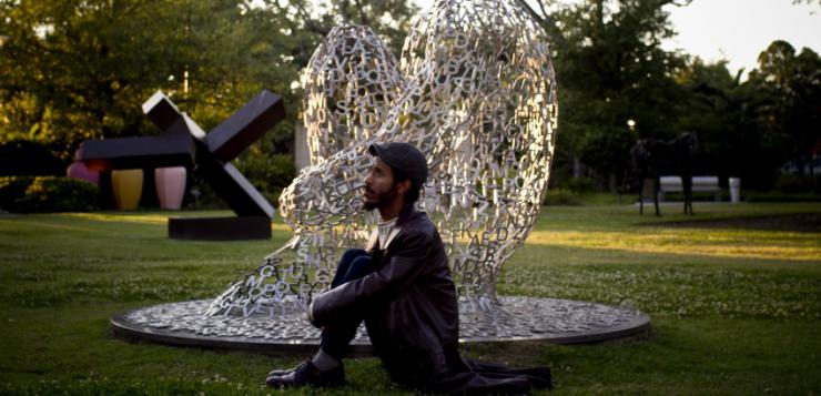 Actor sitting in a sculpture garden.