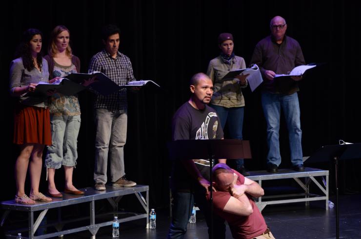 Seven actors in a reading, one actor on their knees
