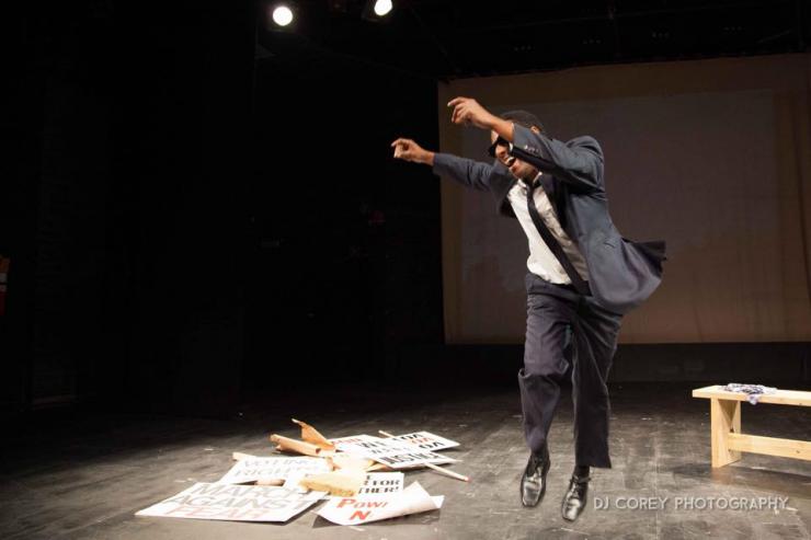 Actor dancing on stage around discarded protest signs