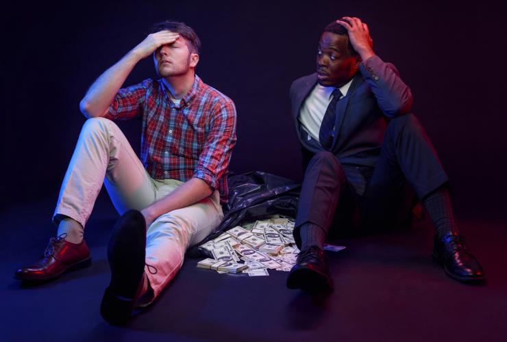 Two actors sitting with a bag of money