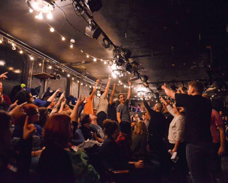 performers and audience pointing to the ceiling of a blackbox theatre