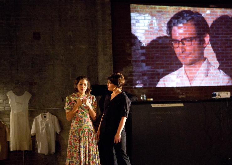 Two actors on stage with a projection 
