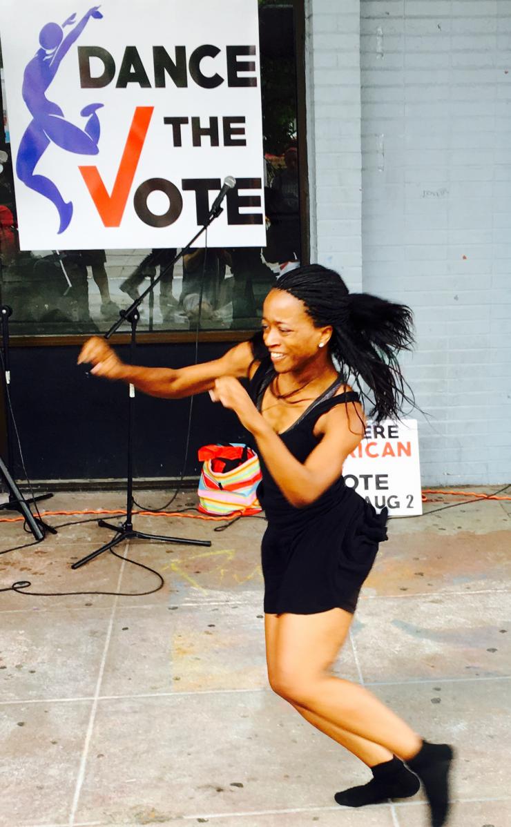A woman dances in front of a sign that says Dance the Vote