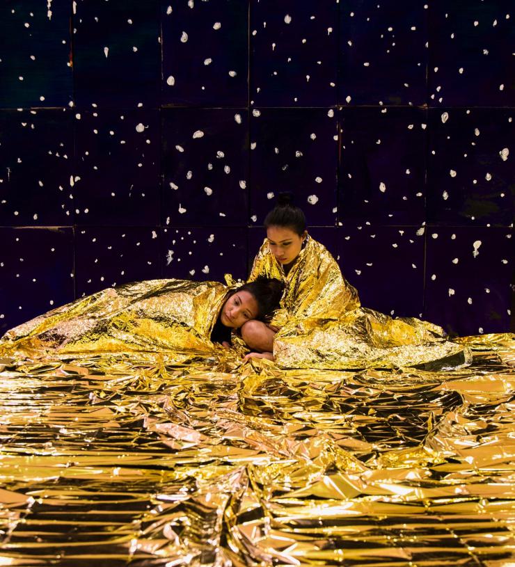 Two actors on stage together in a gold foil blanket
