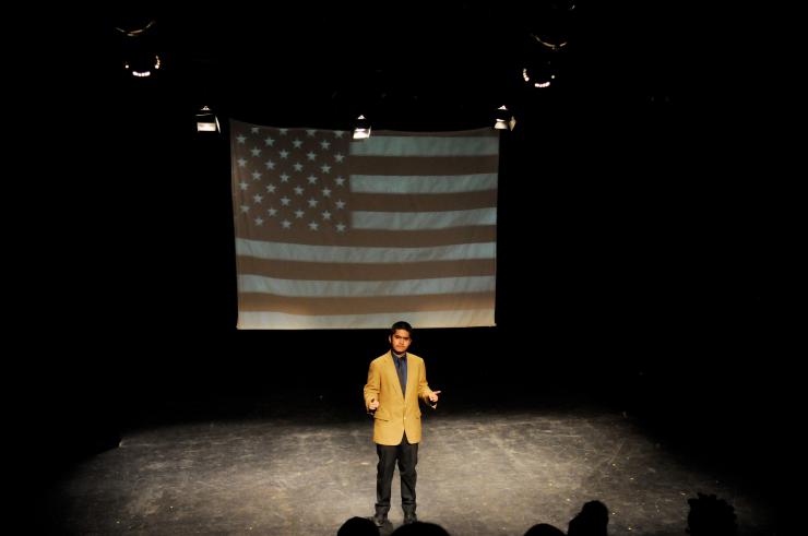 lone actor on stage in front of projection of American flag
