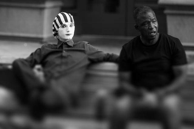 a mime and man sit on a bench