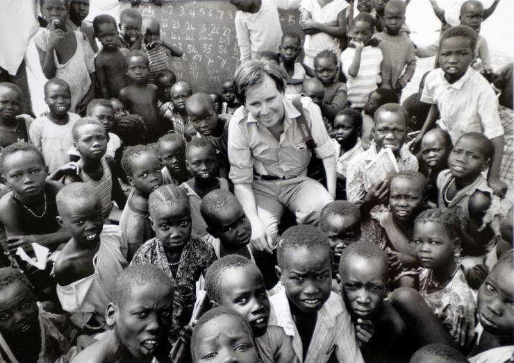 A man sits in the center of a group of children, all are looking at the camera