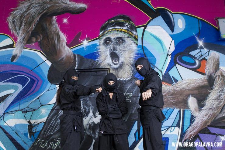 three performers in ninja costumes pose in front of a graffiti wall
