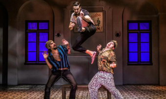 three actors onstage, one jumping in the air.