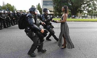black woman in dress stands with arms out in front of uniformed police officers