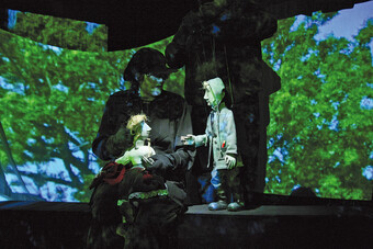 Image of two puppeteers on stage using puppets in front of a digital created forest backdrop. 