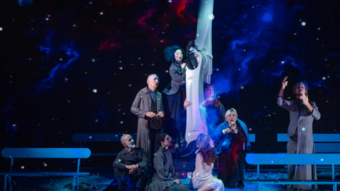 seven performers around large robotic arm in front of a backdrop of the cosmos.