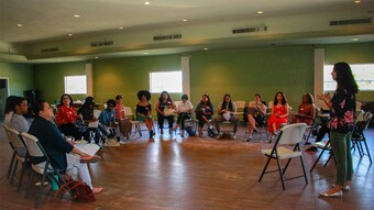 A large group of women sitting in a circle, listening to someone speak.