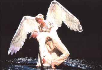 On stage, a performer dressed as an angel holds another performer's limp body.