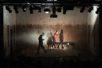 A group of actors perform in a dimly lit space.