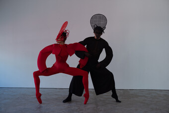 Two figures in abstract red and black costumes dance on stage.