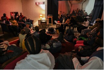 A group of students listen to a radio play in a crowded room.