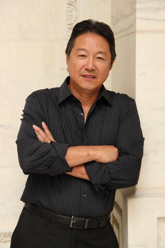 Rick Shiomi leaning on a wall and smiling.