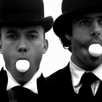 Geoff Sobelle and Trey Lyford in bowler hats blowing bubble gum.