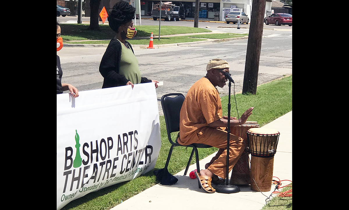 one person seated at a microphone and a drum in front of two people standing with a sign saying Bishop Arts Theatre