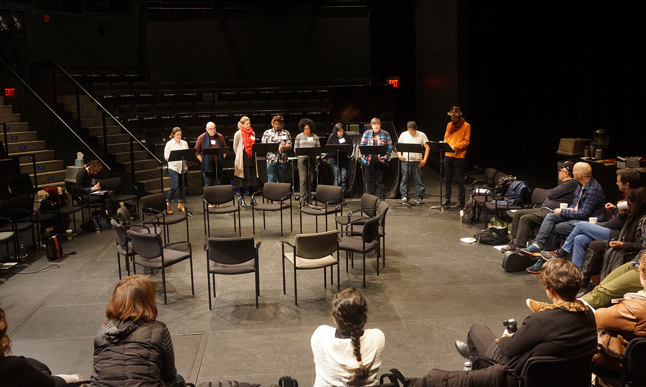 a large group sitting in a circle watching a staged reading