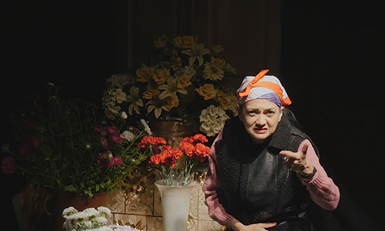 An elderly woman in front of flowers.