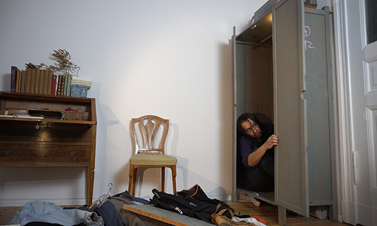 A man peaking out of a cabinet in a apartment room. 
