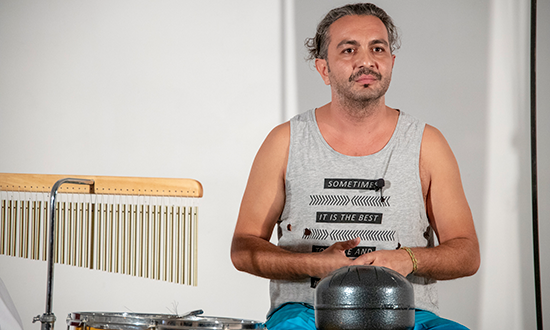 a man in a grey tank top in front of percussion instuments.