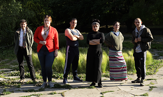 Six performers posing for a picture in a park. 