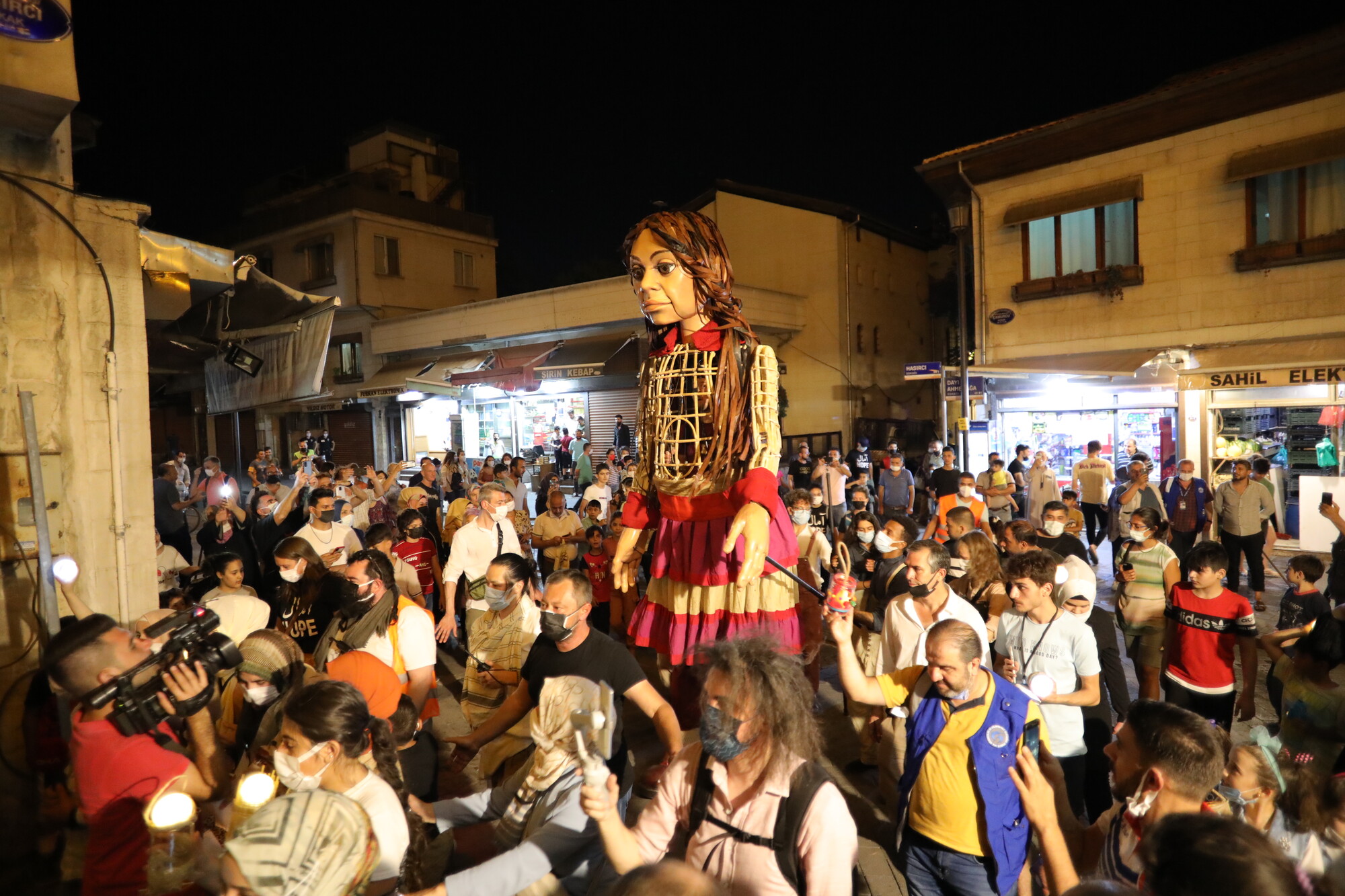 Life-sized internally operated puppet standing in the middle of a crowd.