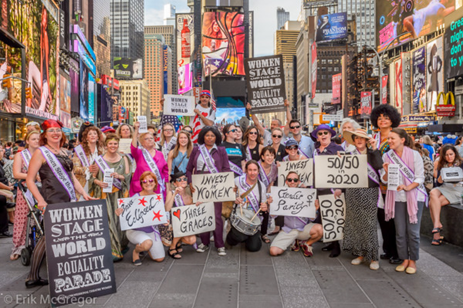 A group of protesters with various posters smile for a photo in Times Square in New York City.