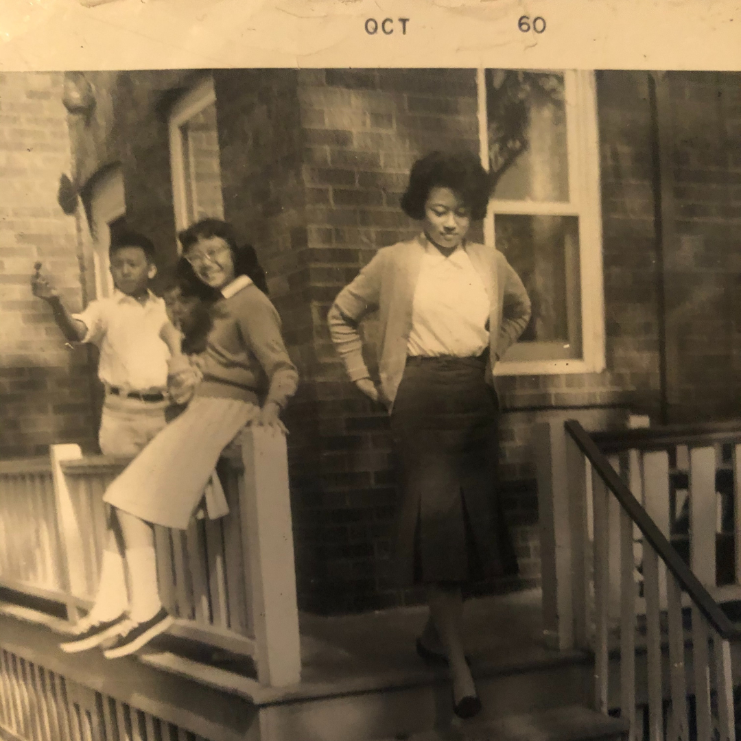 Three young people stand and smile on a front porch.