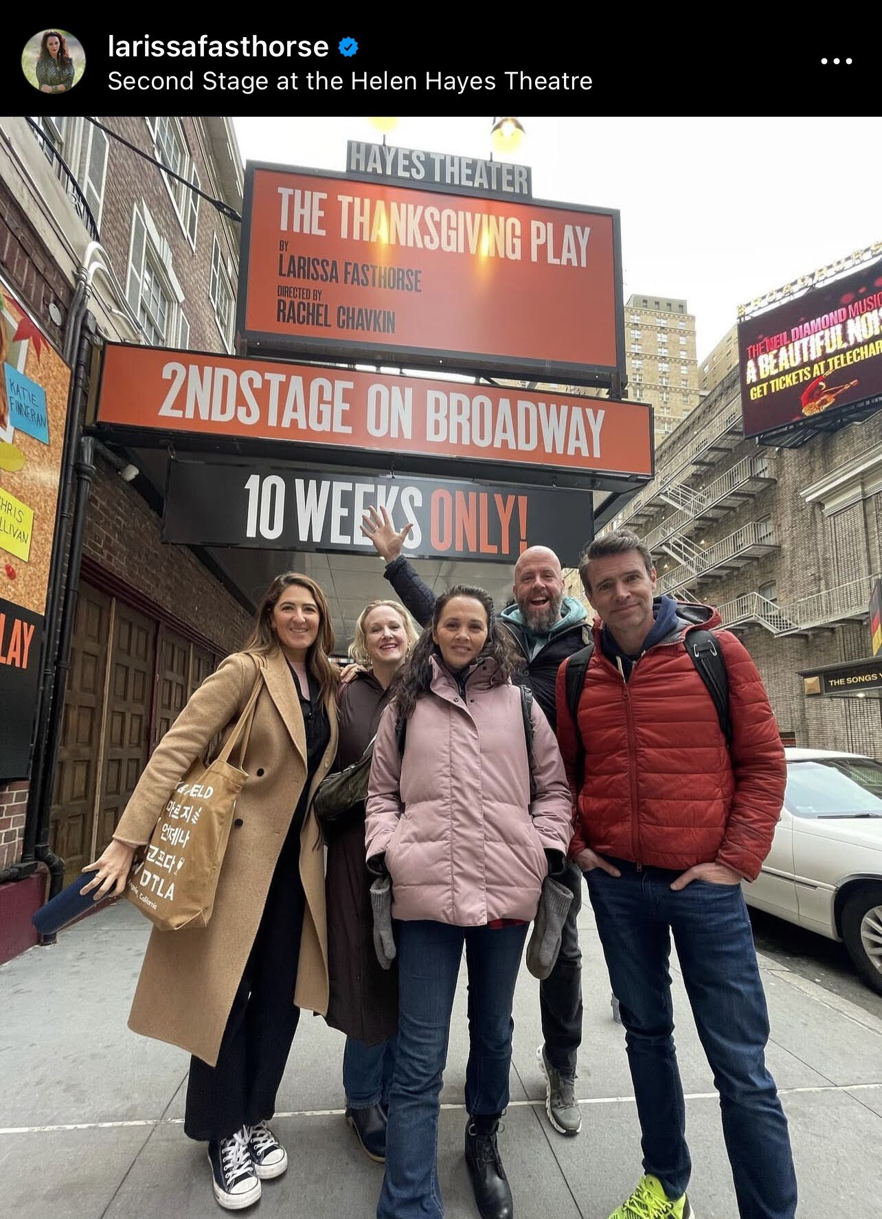 Three woman and two men pose for a picture together on a sidewalk in front of a theatre.