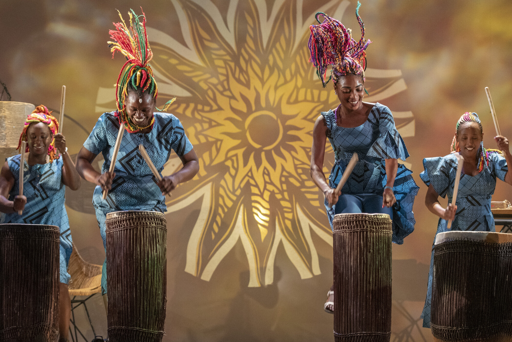 Four women play the drums together on stage.