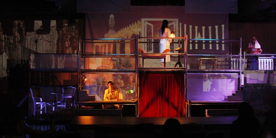 Three actors on a stage with scaffolding, one below and two on top.