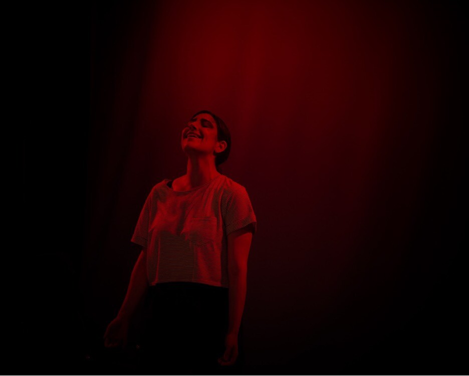 An actor stands dimly lit in red light.