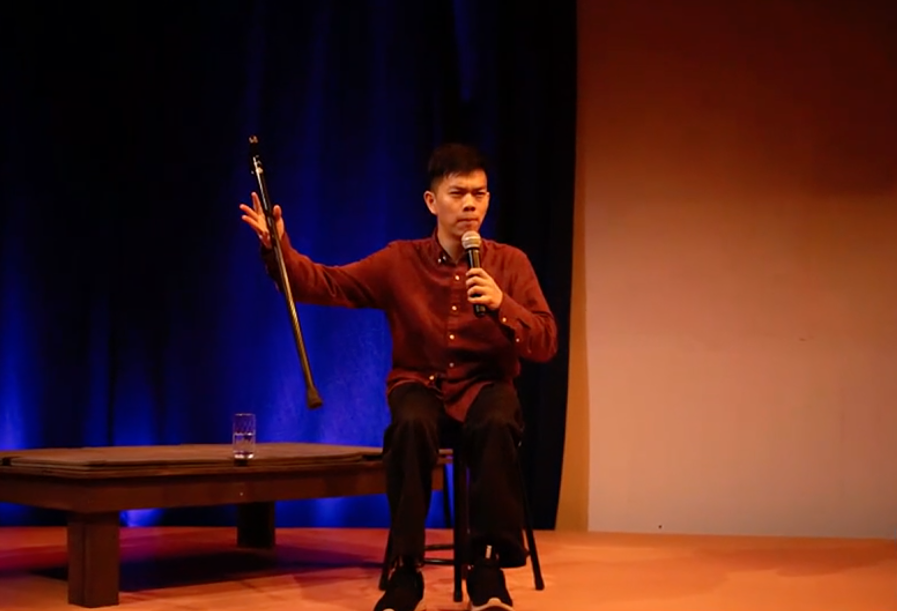 A man in a red shirt stands on stage with a microphone. 